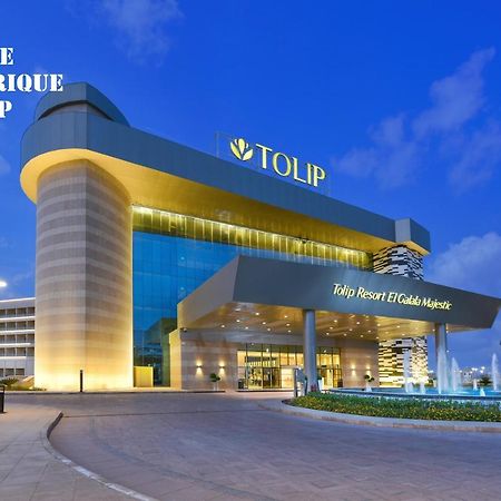 Tolip Resort El Galala Majestic Айн-Сохна Экстерьер фото The photo shows a modern hotel building named "Tolip Resort & Spa," featuring a sleek architectural design with large glass windows. The hotel is illuminated against a twilight sky, showcasing its prominent signage. In the foreground, there is a well