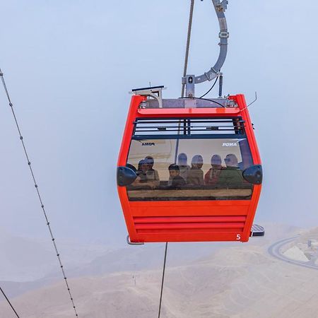 Tolip Resort El Galala Majestic Айн-Сохна Экстерьер фото The photo shows a red gondola lift suspended in the air, traveling along cables. Inside the gondola, a group of people can be seen. The background features a hazy landscape, possibly mountains or hills, indicating an elevated area. The scene conveys 