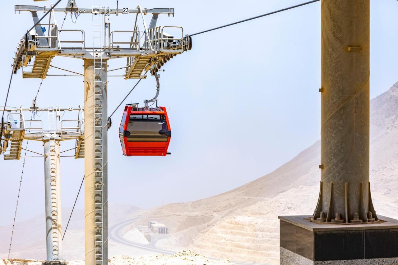 Tolip Resort El Galala Majestic Айн-Сохна Экстерьер фото The photo shows a cable car system with a single red gondola suspended mid-air. It appears to be part of a larger cable car infrastructure, with metal pylons supporting the cables above. The background features a hazy landscape, likely characterized 