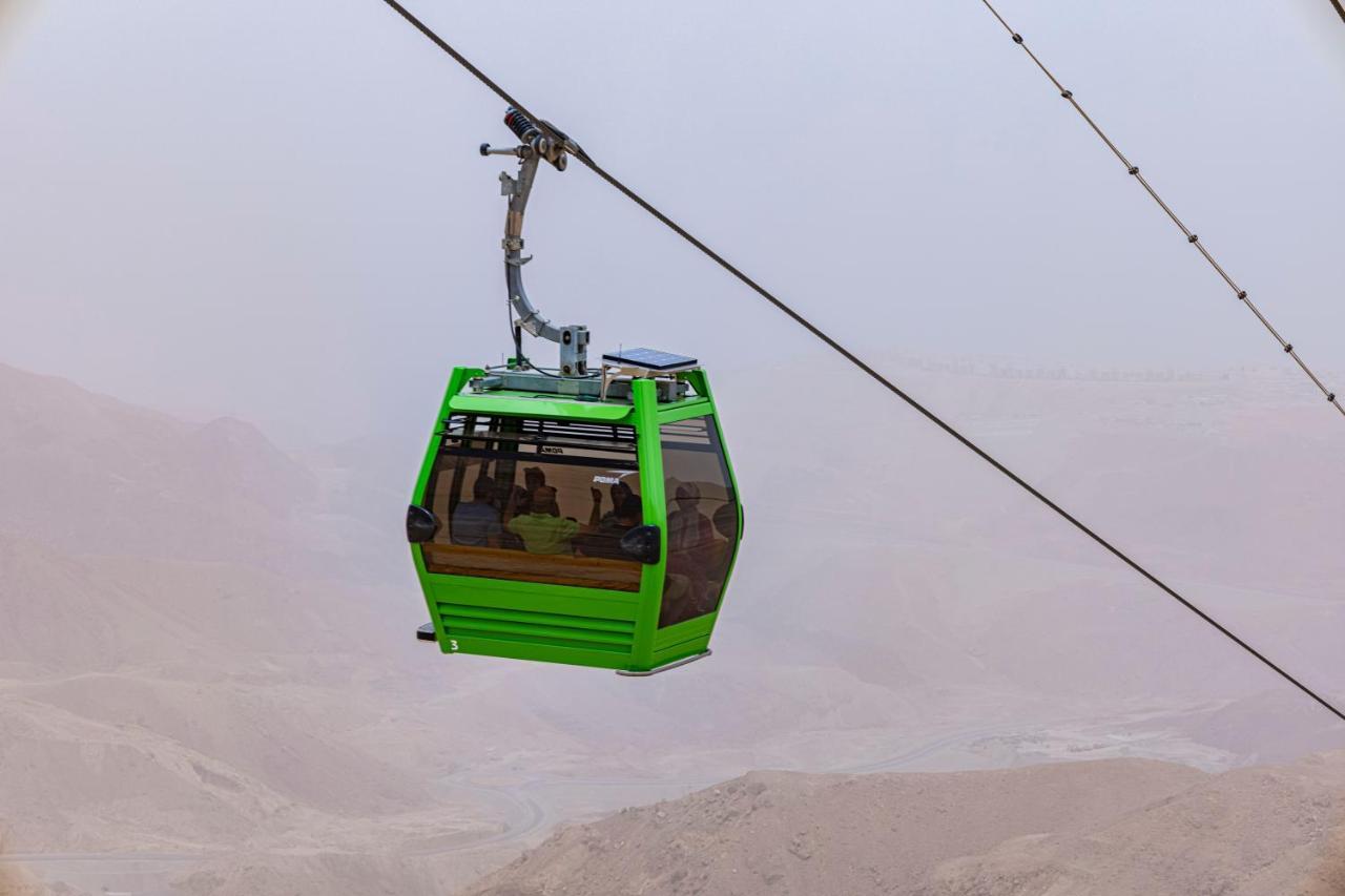 Tolip Resort El Galala Majestic Айн-Сохна Экстерьер фото The photo shows a green cable car suspended in the air, moving along a wire. The cable car appears to be traversing a mountainous landscape, which looks rocky and arid. The surrounding environment is somewhat foggy or hazy, suggesting limited visibil