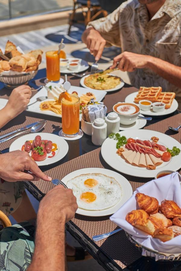 Tolip Resort El Galala Majestic Айн-Сохна Экстерьер фото The photo features a spread of breakfast dishes on a table. There are two sunny-side-up eggs on one plate, surrounded by various food items, including slices of ham, sausages, and fresh tomatoes. Another plate holds a serving of waffles. A bowl with 