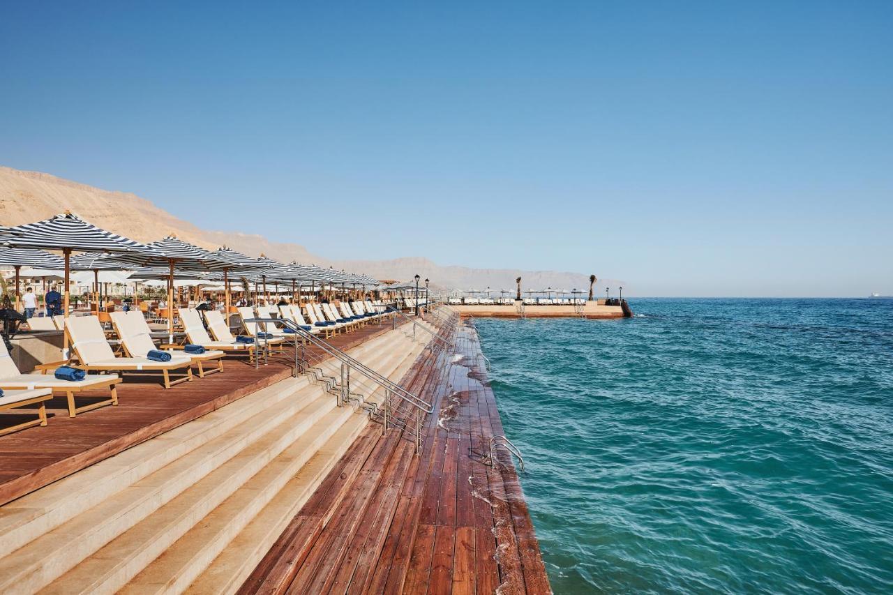 Tolip Resort El Galala Majestic Айн-Сохна Экстерьер фото The photo shows a seaside area featuring a wooden deck that extends into the water. On the left side, there are several lounge chairs arranged neatly under shade structures, suggesting a relaxing atmosphere. The ocean is visible in the foreground, wi