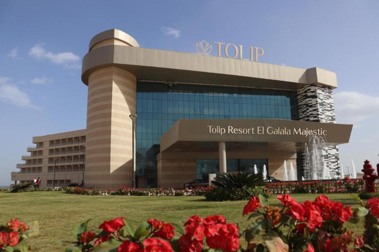 Tolip Resort El Galala Majestic Айн-Сохна Экстерьер фото The photo shows a modern hotel building named "Tolip Resort El Galala Majestic." The structure features a distinctive architectural design with large glass windows and a prominent entrance. Surrounding the building are well-maintained lawns and vibra