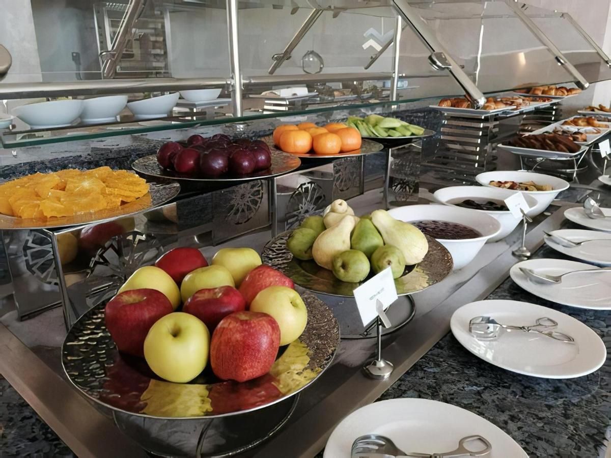 Tolip Resort El Galala Majestic Айн-Сохна Экстерьер фото The photo displays a buffet setup featuring an assortment of fresh fruits arranged on several tiered trays. There are red and green apples, pears, grapes, and oranges. Adjacent to the fruit display, there are several bowls containing various other fo