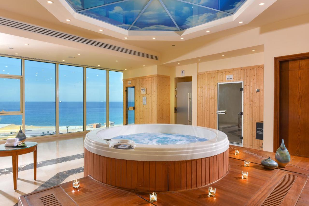 Tolip Resort El Galala Majestic Айн-Сохна Экстерьер фото The photo shows a luxurious spa room featuring a large, round hot tub positioned in the center. The walls are mostly glass, offering a stunning view of the ocean. The ceiling has a painted sky, enhancing the serene atmosphere. There are wooden elemen